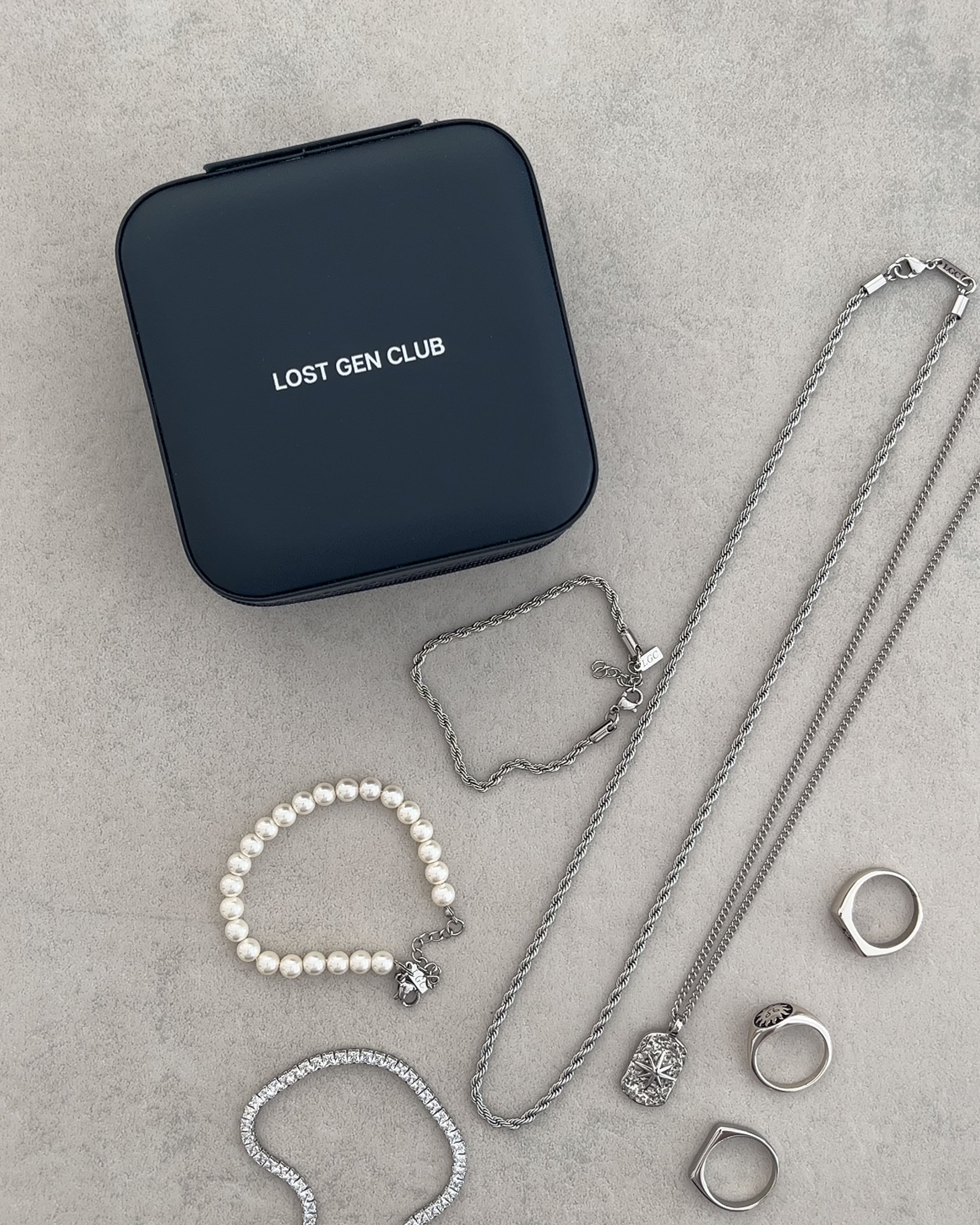 Dark blue square jewelry case with Lost Gen Club branding on a textured surface beside silver chains.