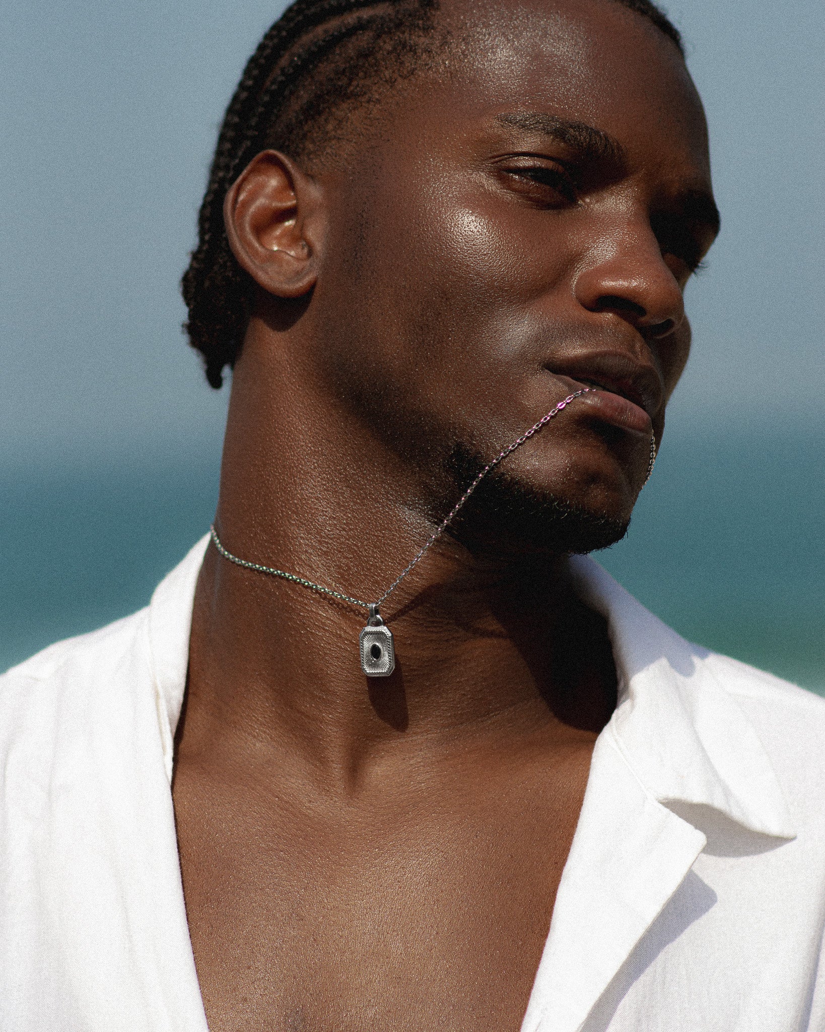 Close-up of a silver pendant necklace on a model's neck against a pale blue backdrop.