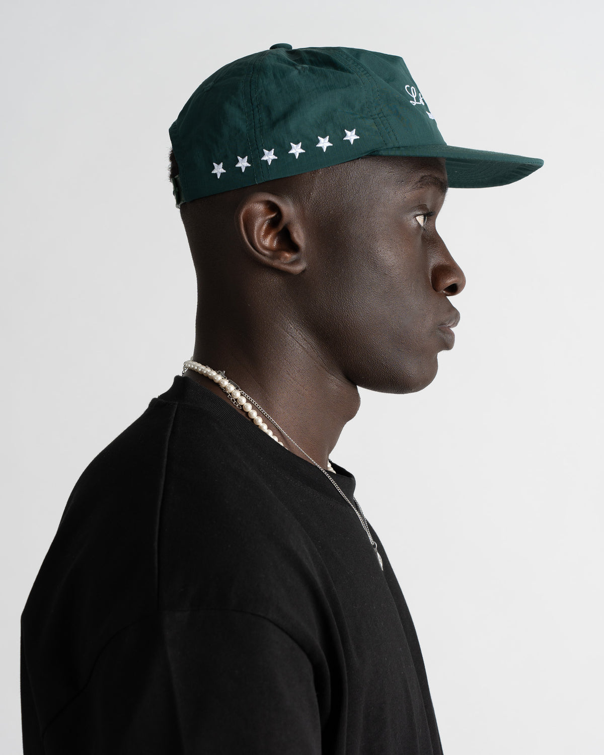 Profile view of a green nylon five panel cap worn by a model with white star embroidery along the back panel.