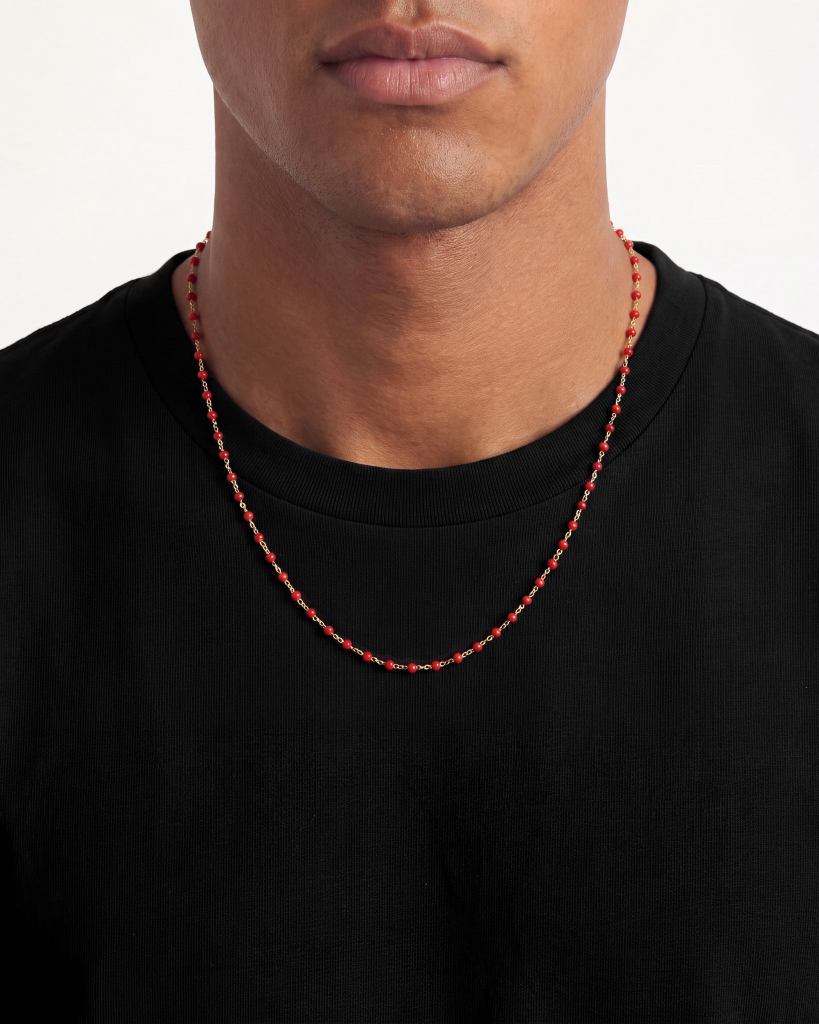 Gold chain necklace with red beads resting on a black shirt
