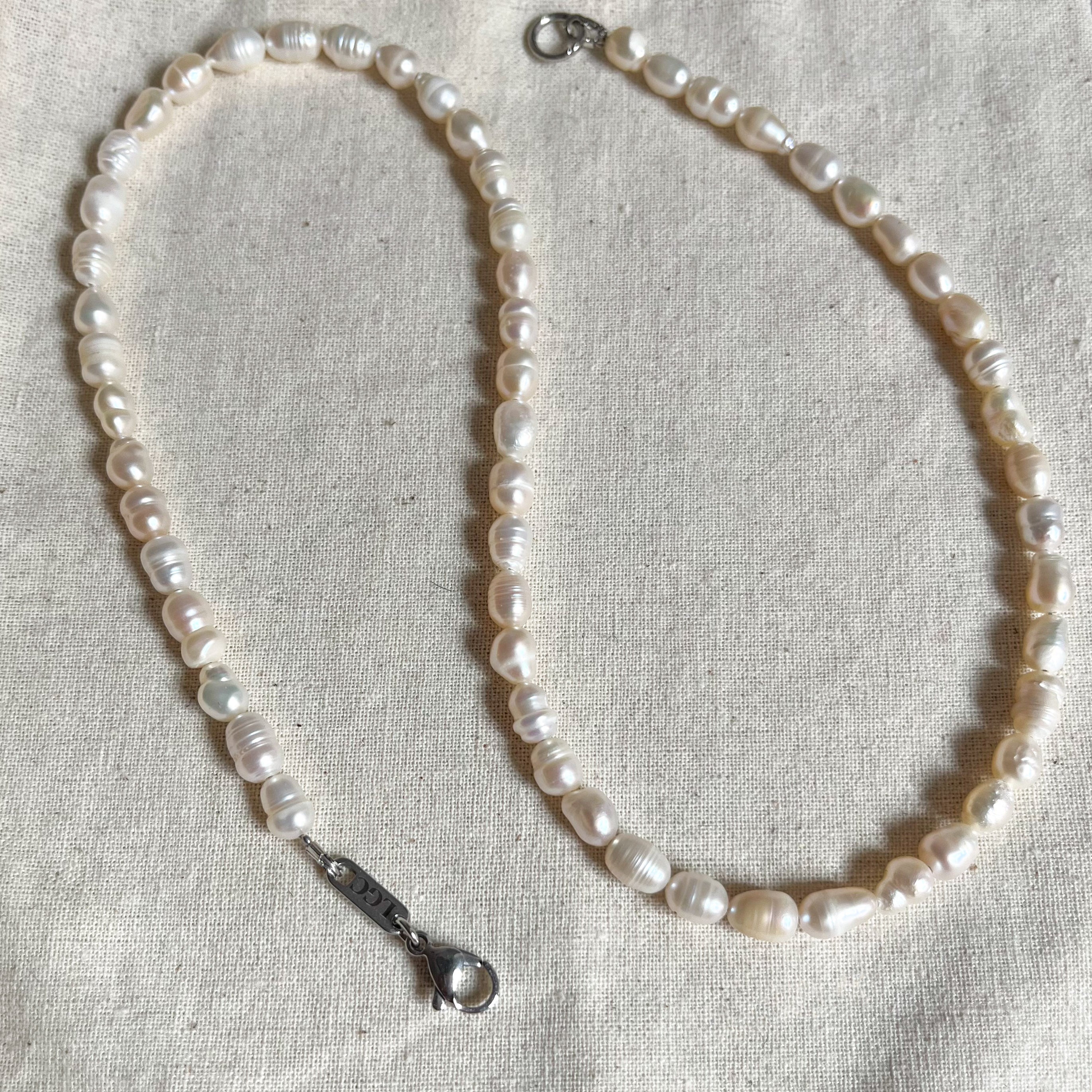 Cadenas de perlas blancas irregulares sobre tela beige, con broche plateado visible