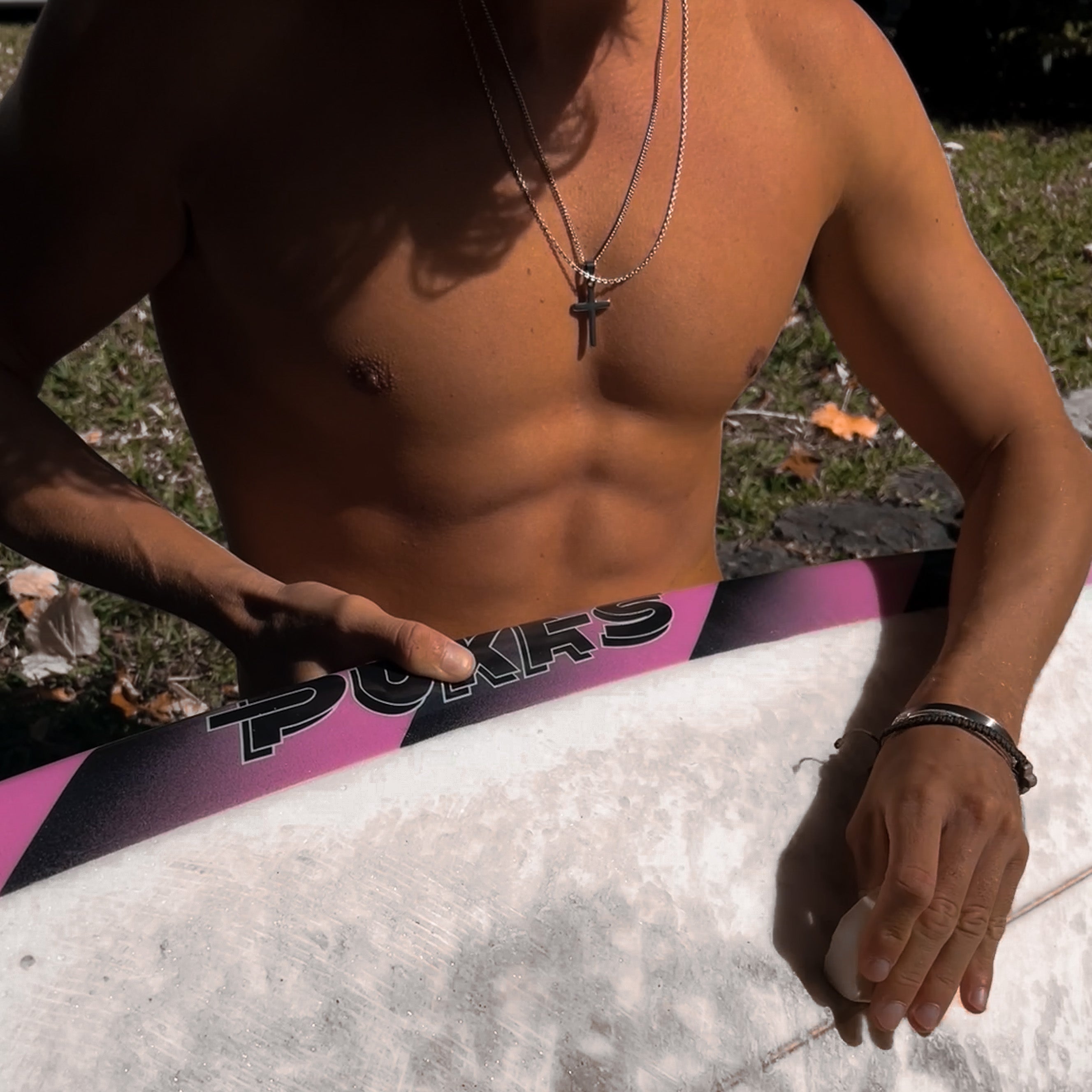 Man shirtless outdoors wearing layered necklaces with a cross pendant.
