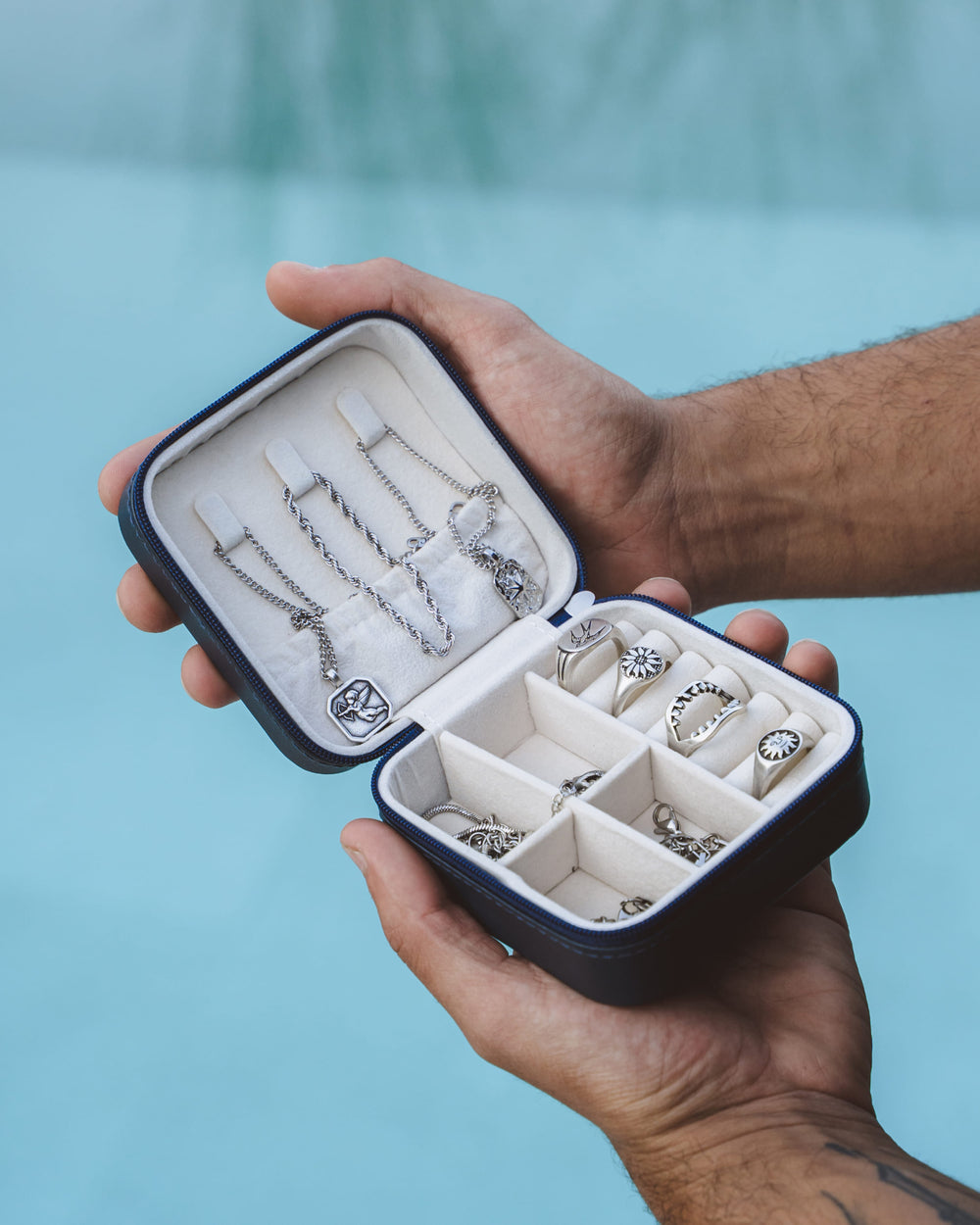 Open jewelry box showing a selection of silver chains and rings arranged in compartments.