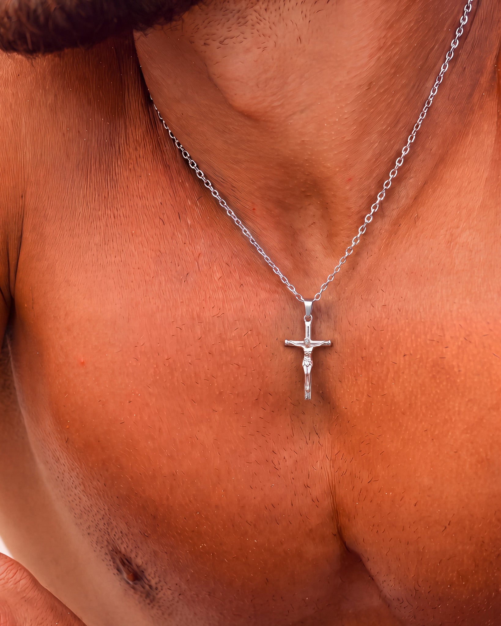 Silver crucifix necklace worn around the neck with pendant resting at the collarbone