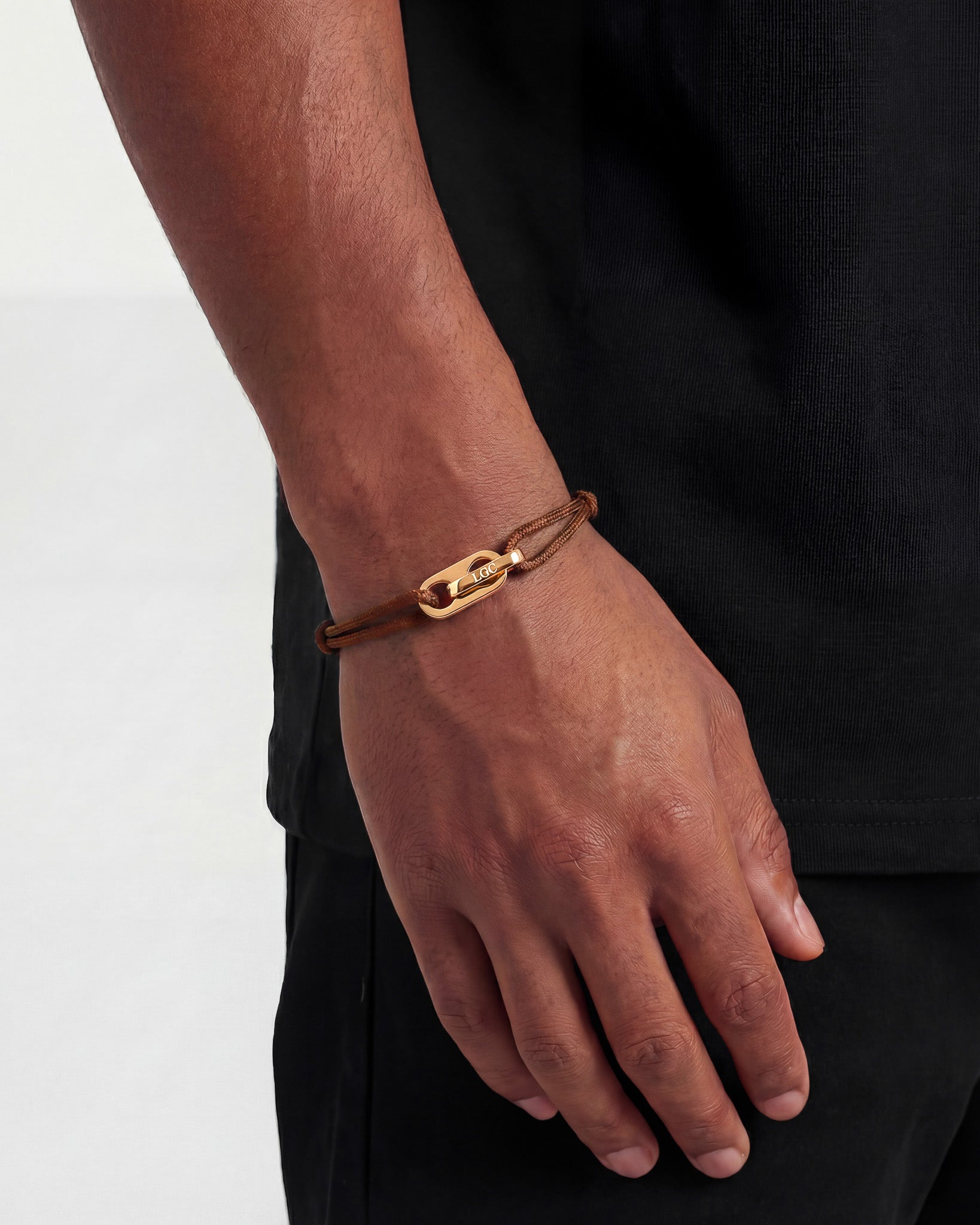 Atlantis gold bracelet worn on the wrist with a brown braided cord and a gold clasp.