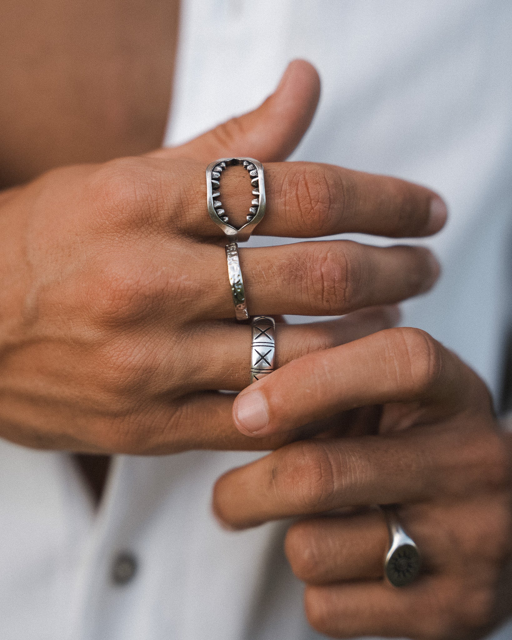 Hammered silver ring with an open square face and jagged inner edge worn on the finger.