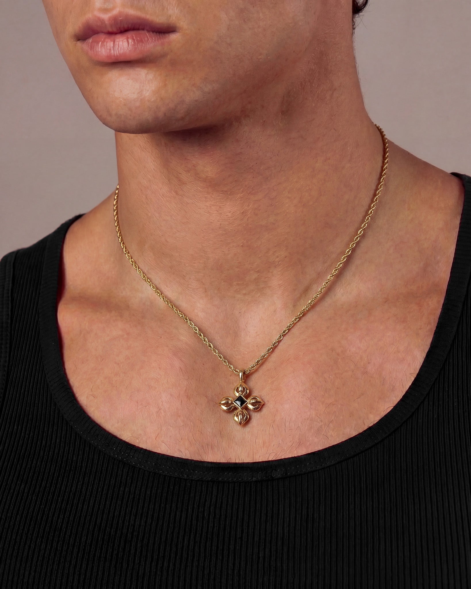 Gold tone necklace with twisted chain and a four petal cross pendant on a model's neck
