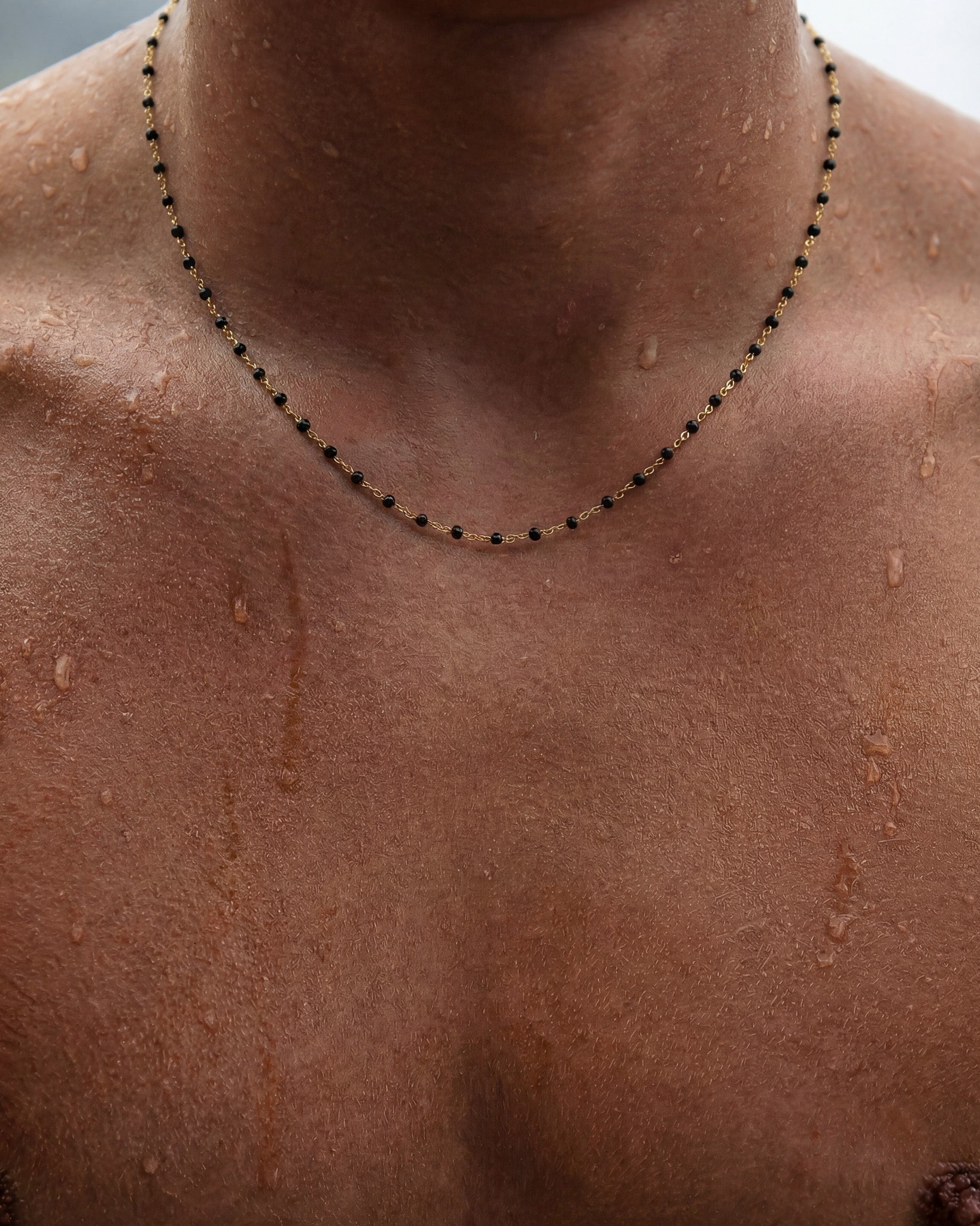 Gold chain necklace with black beads draped around a model's neck.