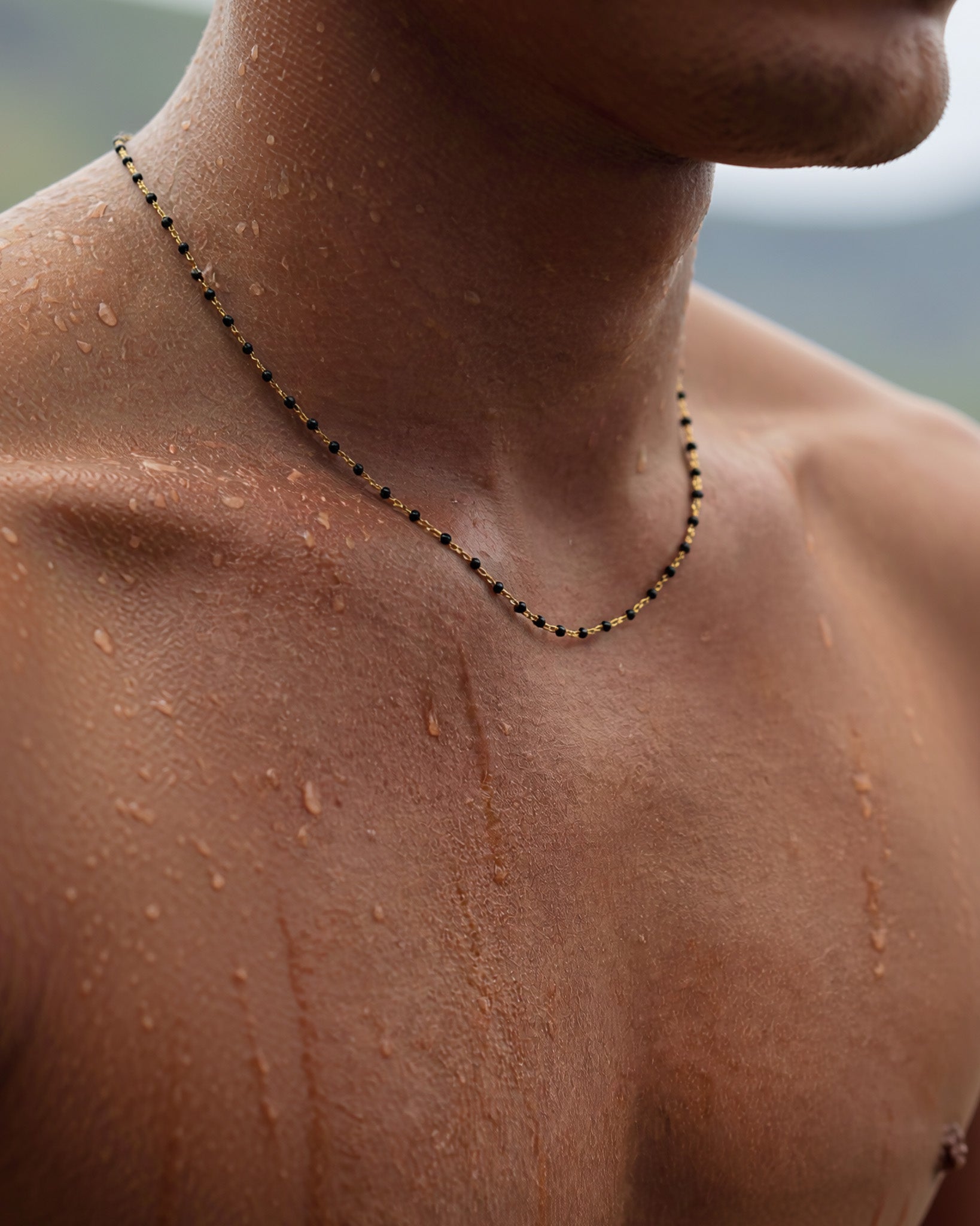 GEM GOLD CHAIN necklace with alternating small black beads on a delicate gold chain draped over a wet neck