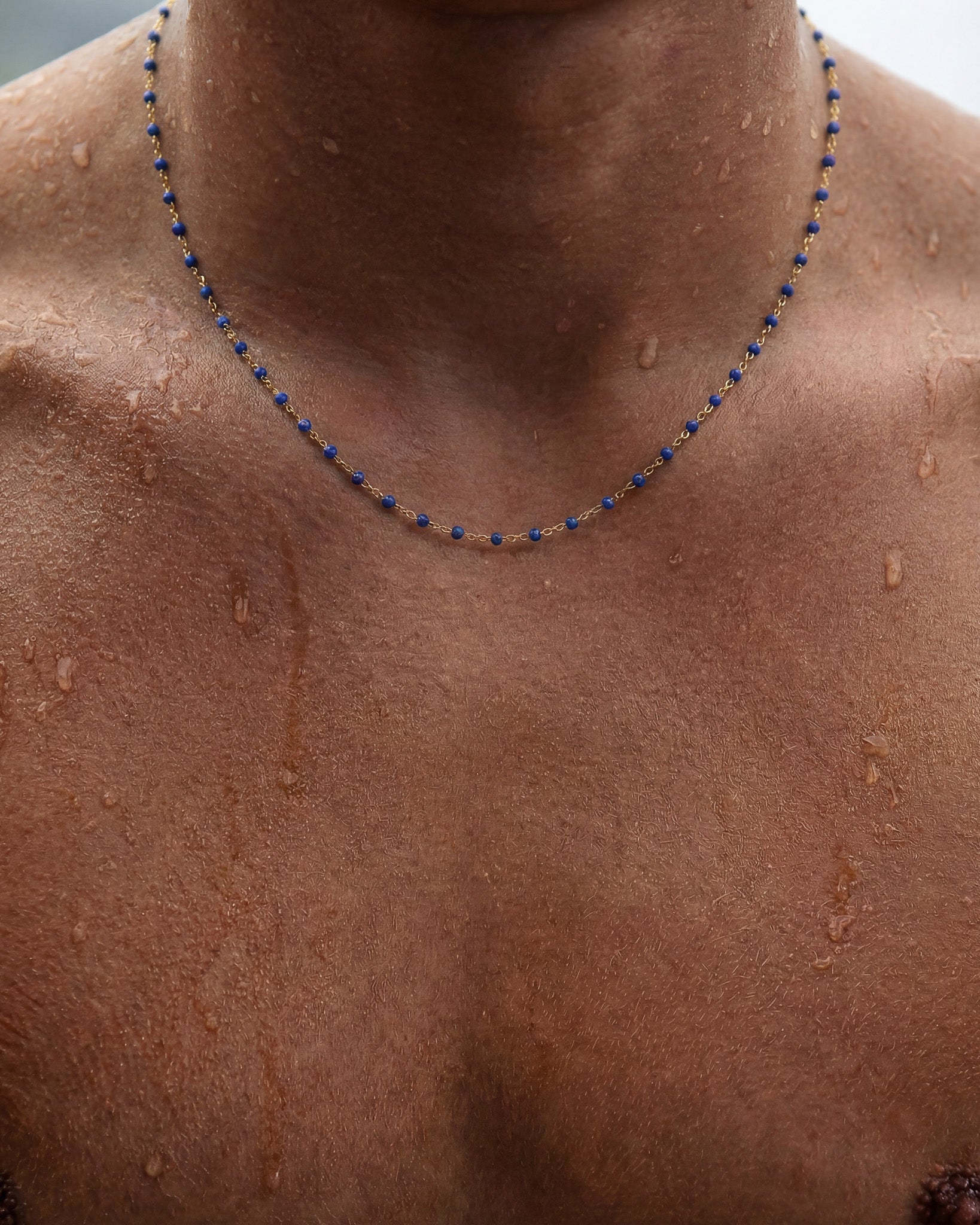 GEM GOLD CHAIN necklace with blue beads along a gold chain draped around the neck on wet skin