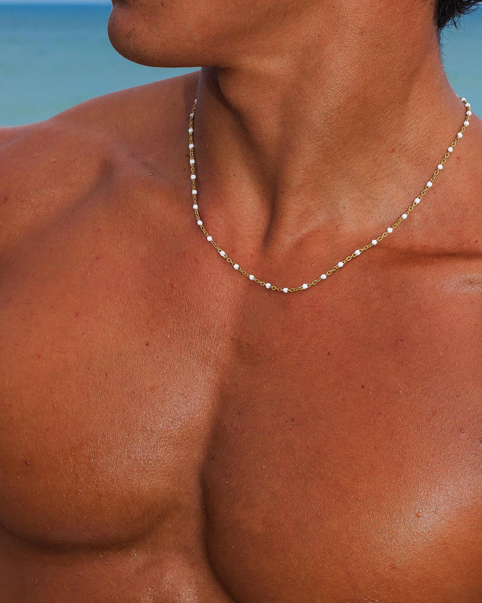 Gold chain necklace with small white beads draped over a tanned chest