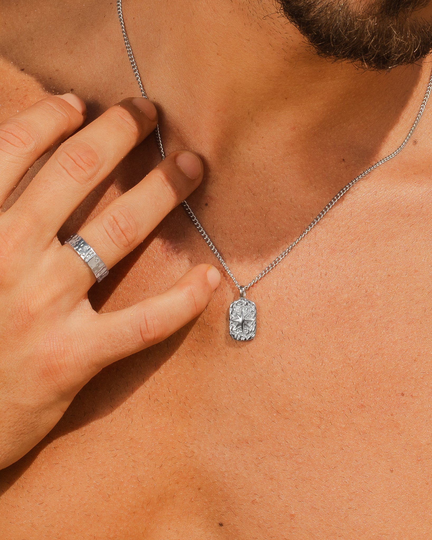 Close up of hammered silver 6mm ring on a finger and a silver chain necklace with a square pendant resting on the chest.
