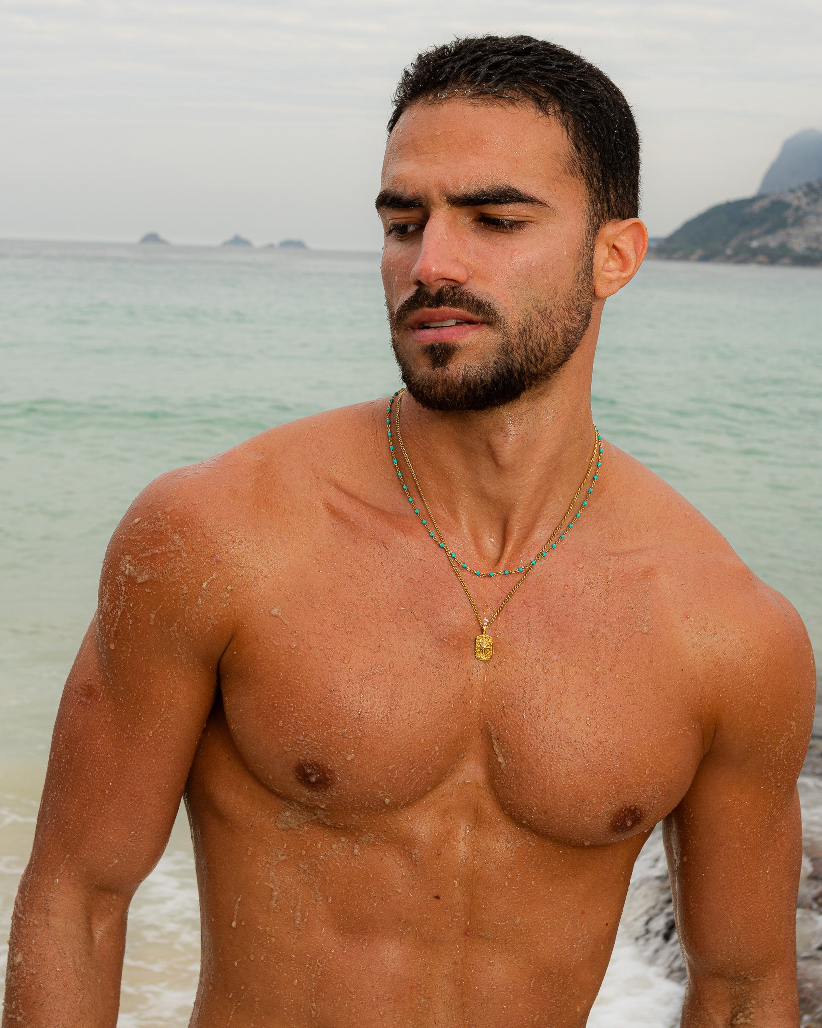 Man wearing turquoise beaded necklace and a second gold chain with a square pendant at the chest