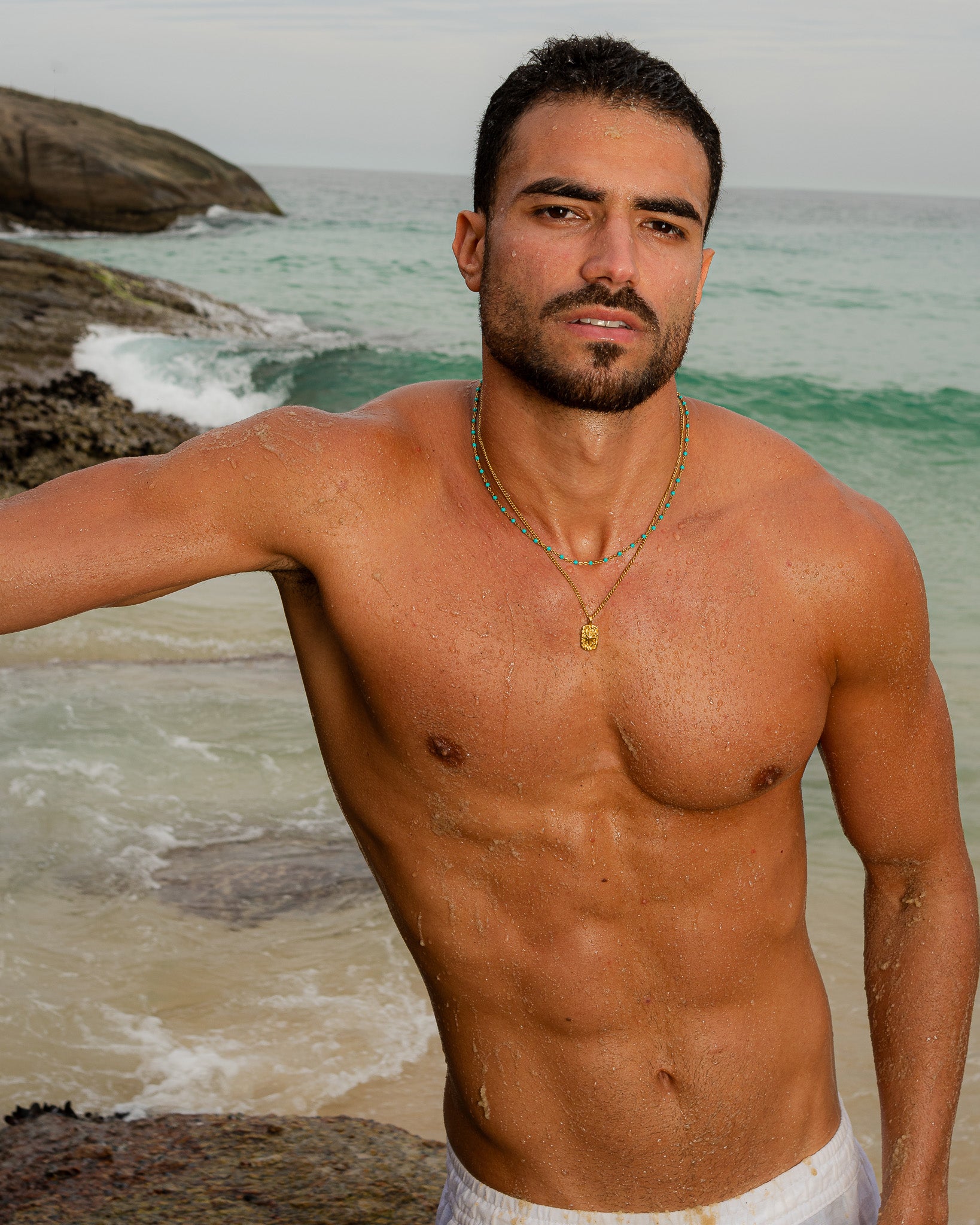 Turquoise bead and gold chain around a man's neck at the beach