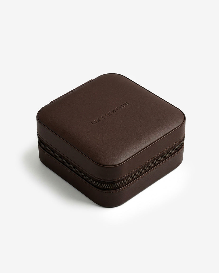 Brown leather travel jewelry case closed, with LOST GEN CLUB embossed on the lid and a zip around the edge